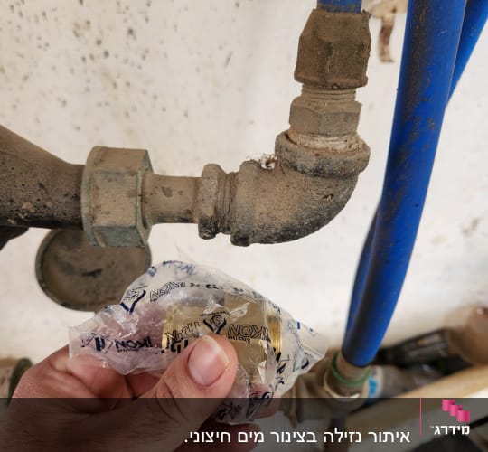 יד מחזיקה חלק פלסטיק ליד צינורות מים כחולים
